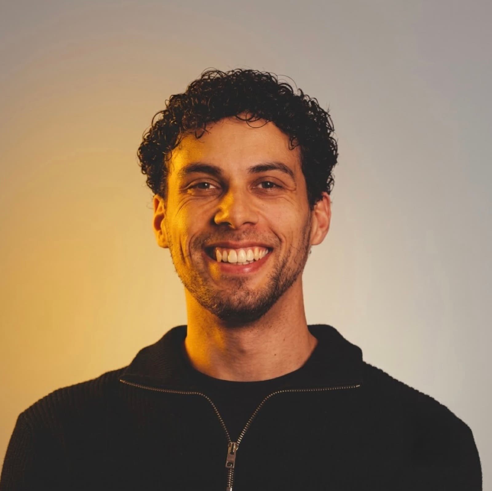Karim, lachend in een zwarte trui tegen een goudkleurige achtergrond